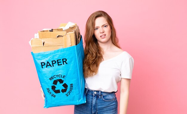 Mulher bonita ruiva se sentindo perplexa e confusa e segurando um saco de papel reciclado