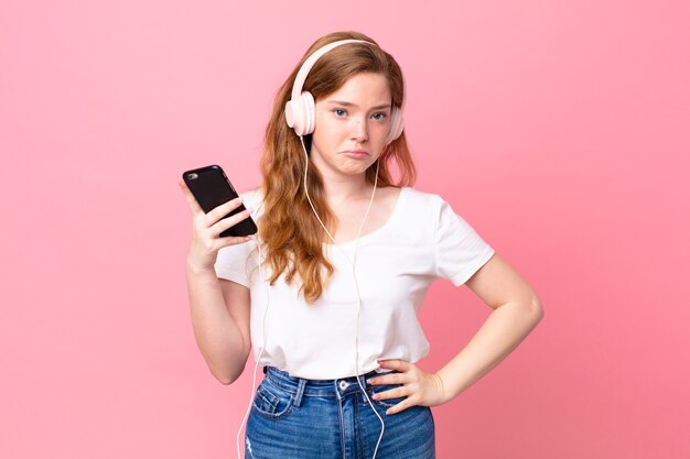 Mulher bonita ruiva se sentindo triste e chorona com um olhar infeliz e chorando com fones de ouvido e smartphone