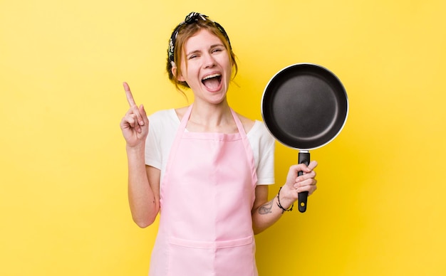 Mulher bonita ruiva se sentindo um gênio feliz e animado depois de perceber uma ideia de frigideira e conceito de dona de casa