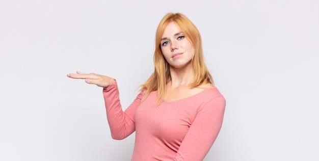 Mulher bonita ruiva segurando um objeto com as duas mãos no espaço lateral da cópia, mostrando, oferecendo ou anunciando um objeto