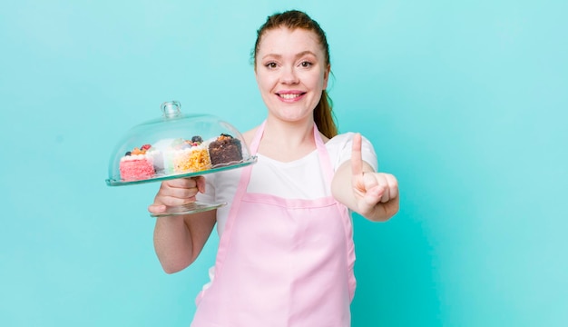 Mulher bonita ruiva sorrindo com orgulho e confiança, fazendo o conceito número um de bolos caseiros