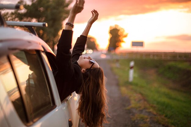 Foto mulher bonita se inclinando da janela do carro durante o pôr do sol