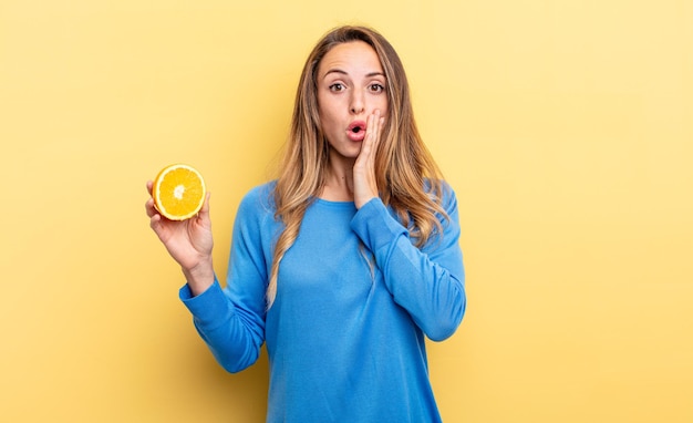 Mulher bonita se sentindo chocada e assustada segurando meia laranja