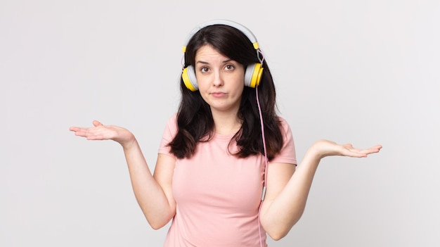 Mulher bonita se sentindo confusa e confusa e duvidando de ouvir música com fones de ouvido