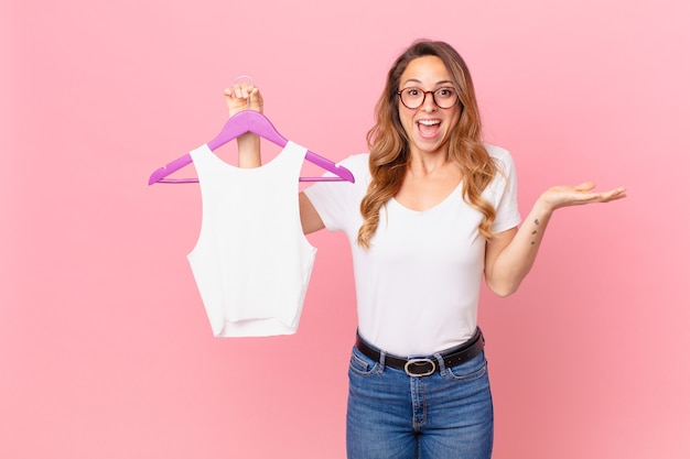 Mulher bonita se sentindo feliz e surpresa com algo inacreditável e escolhendo roupas