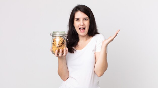 Mulher bonita se sentindo feliz e surpresa com algo inacreditável e segurando uma garrafa de vidro de biscoitos