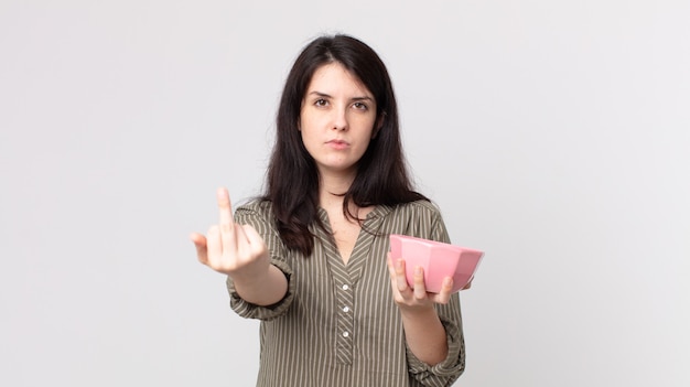 Mulher bonita se sentindo irritada, irritada, rebelde e agressiva segurando uma tigela de panela vazia. agente assistente com fone de ouvido