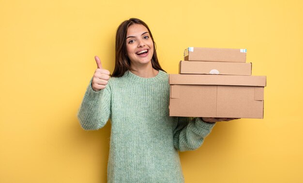 Mulher bonita se sentindo orgulhosa, sorrindo positivamente com polegares para cima conceito de caixas de pacotes