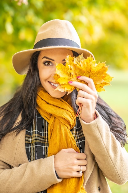 Mulher bonita segura folhas de outono coloridas na frente de um de seus olhos em um dia frio de outono.