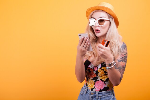 Mulher bonita segurando telefone inteligente e cartão de crédito no estúdio em fundo amarelo