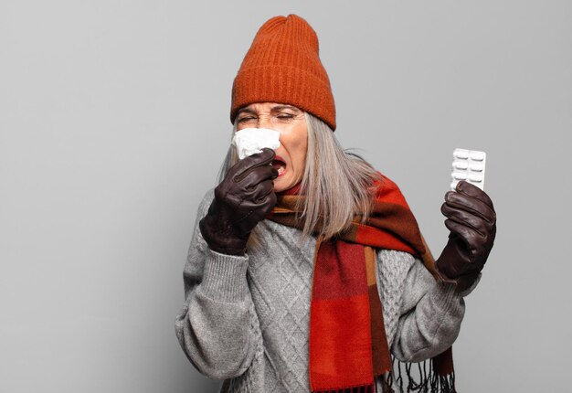 Foto mulher bonita sênior com um comprimido de comprimidos, vestindo roupas de inverno. conceito de gripe
