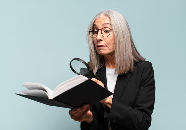 Mulher bonita sênior com um livro e uma lupa. conceito de pesquisa