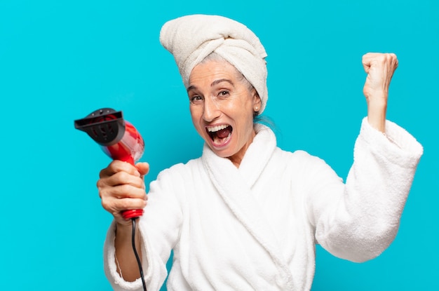 Mulher bonita sênior depois do banho, vestindo um roupão de banho. conceito de secador de cabelo