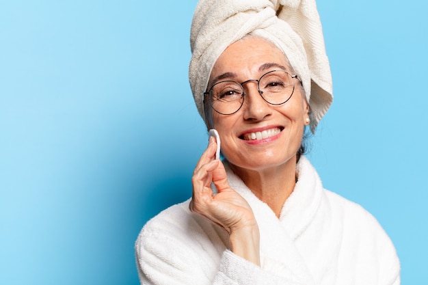 Mulher bonita sênior fazendo limpeza facial ou maquiagem após o banho de roupão