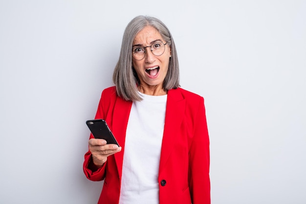 Mulher bonita sênior parecendo muito chocada ou surpresa... conceito de negócios e telefone