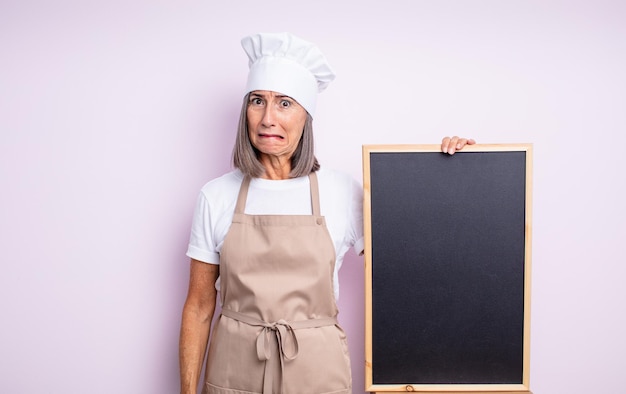 Mulher bonita sênior parecendo perplexa e confusa. conceito de chef e quadro-negro