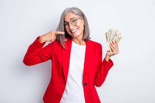 Mulher bonita sênior sorrindo com confiança, apontando para o próprio sorriso largo. conceito de negócios e notas