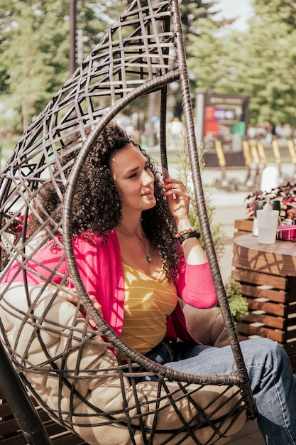 Mulher bonita sentada em uma rede de vime em um café na rua, esperando por uma reunião e um encontro