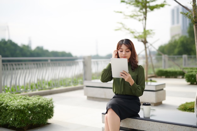 Mulher bonita sentada no banco usando o tablet ao ar livre.