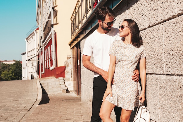 Foto mulher bonita sorridente e seu namorado bonito mulher em roupas casuais de verão família alegre feliz mulher se divertindo casal posando no fundo da rua em óculos de sol abraçando um ao outro