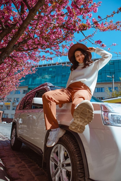 Mulher bonita sorridente elegante parada perto da árvore de sakura florescendo carro no fundo