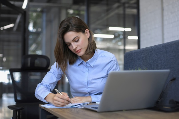 Foto mulher bonita sorridente se senta à mesa. feliz empresário escreve notas aos clientes.