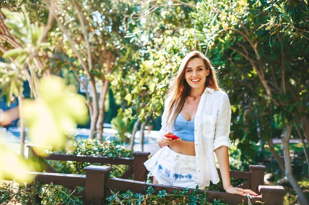 Mulher bonita sorridente segurando e usando smartphone para conversar em busca de mensagens de texto