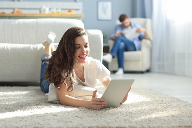 Foto mulher bonita sorridente usando laptop com homem borrado no fundo em casa.