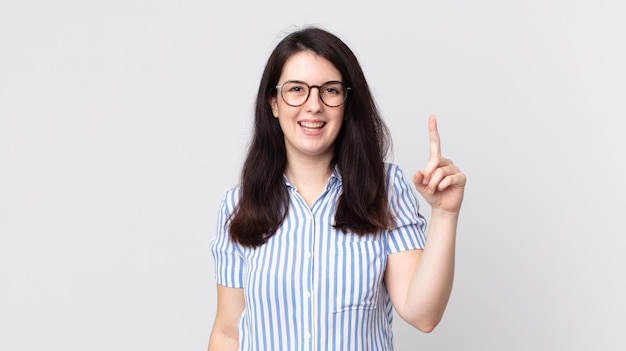 Mulher bonita sorrindo alegre e feliz, apontando para cima com uma mão para copiar o espaço