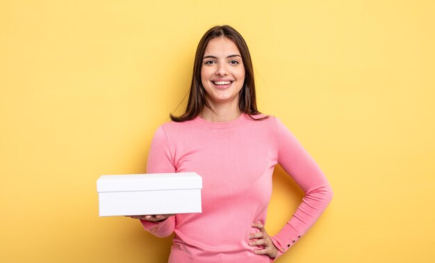 mulher bonita sorrindo alegremente com uma mão no quadril e confiante. conceito de embalagem de caixa branca