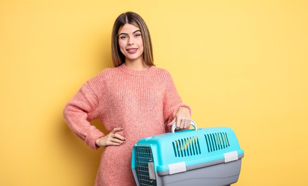 Mulher bonita sorrindo alegremente com uma mão no quadril e confiante. conceito de pet transportadora