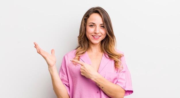 Mulher bonita sorrindo alegremente e apontando para copiar o espaço na palma da mão mostrando ou anunciando um objeto