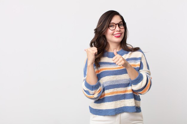 Mulher bonita sorrindo alegremente e casualmente apontando para copiar o espaço ao lado, sentindo-se feliz e satisfeita