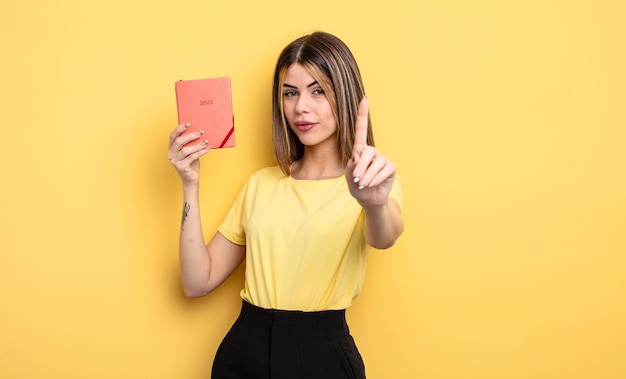 Mulher bonita sorrindo com orgulho e confiança fazendo o número um. conceito de planejador