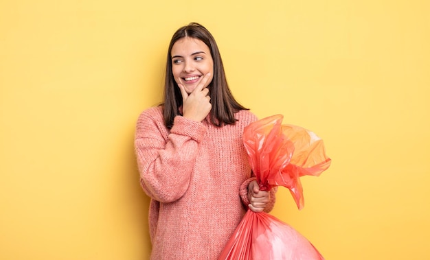 Mulher bonita sorrindo com uma expressão feliz e confiante com a mão no queixo. conceito de saco de lixo