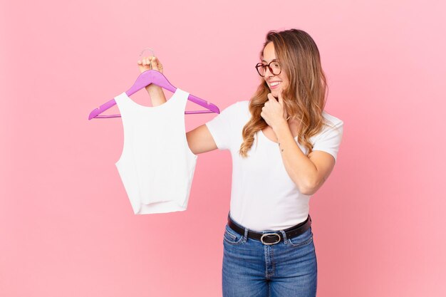 Mulher bonita sorrindo com uma expressão feliz e confiante com a mão no queixo e escolhendo roupas