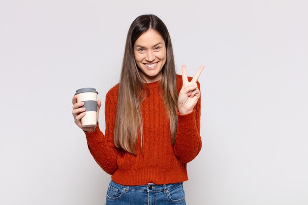 Mulher bonita sorrindo e parecendo amigável, mostrando o número dois ou o segundo com a mão para a frente, em contagem regressiva