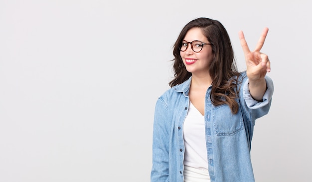 Mulher bonita sorrindo e parecendo amigável, mostrando o número dois ou o segundo com a mão para a frente, em contagem regressiva