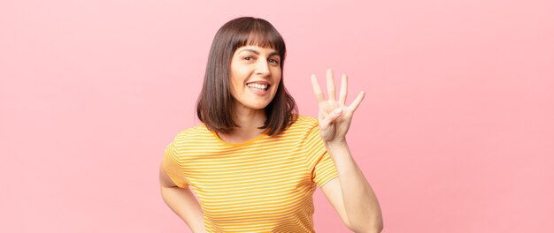 Mulher bonita sorrindo e parecendo amigável, mostrando o número quatro ou o quarto com a mão para a frente, em contagem regressiva