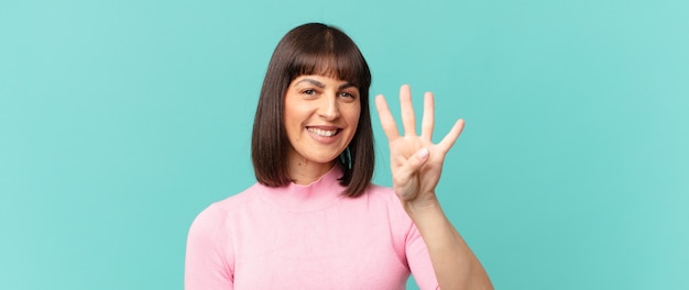 Mulher bonita sorrindo e parecendo amigável, mostrando o número quatro ou o quarto com a mão para a frente, em contagem regressiva