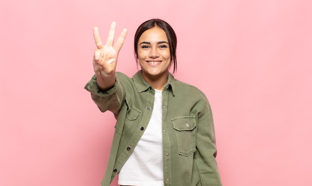 Mulher bonita sorrindo e parecendo amigável, mostrando o número três ou o terceiro com a mão para a frente, em contagem regressiva