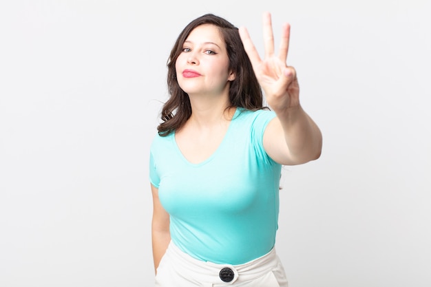 Mulher bonita sorrindo e parecendo amigável, mostrando o número três ou terceiro com a mão para a frente, em contagem regressiva