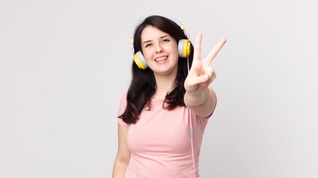 Mulher bonita sorrindo e parecendo feliz, gesticulando vitória ou paz ouvindo música com fones de ouvido