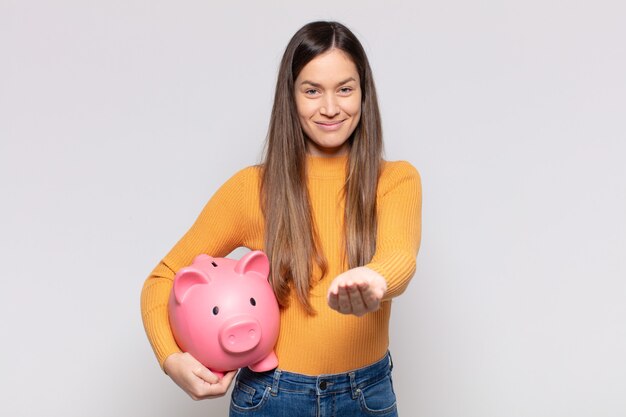 Mulher bonita sorrindo feliz com um olhar amigável, confiante e positivo, oferecendo e mostrando um objeto ou conceito