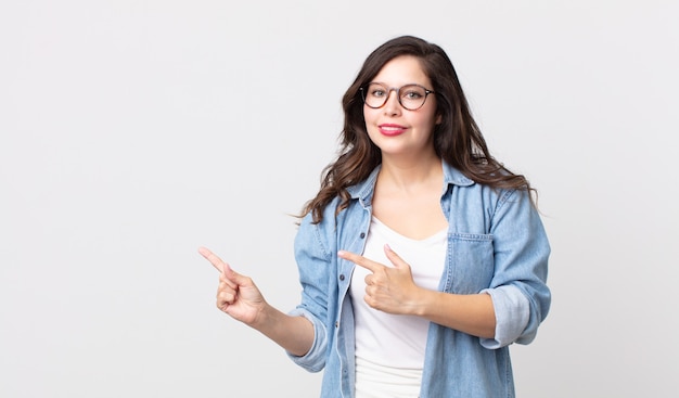 Mulher bonita sorrindo feliz e apontando para o lado e para cima com as duas mãos mostrando o objeto no espaço da cópia