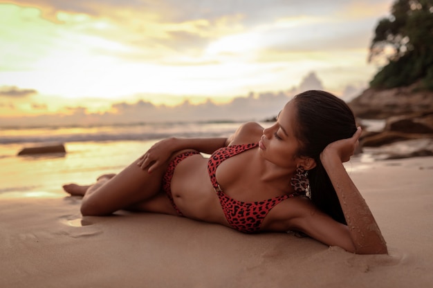 Mulher bonita tailandesa com corpo perfeito, deitado na areia e apreciando o pôr do sol do mar nas férias de verão