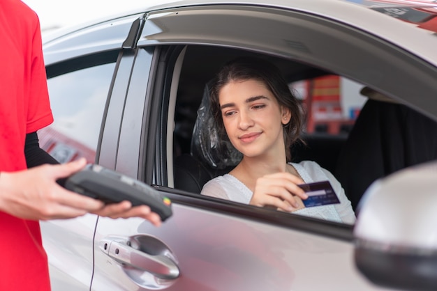 Mulher bonita usando cartão de crédito com terminal de pagamento com cartão para pagar reabastecimento de gasolina no posto de gasolina