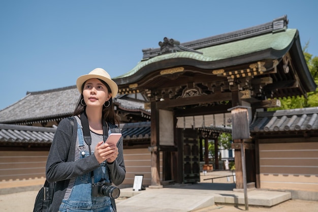 mulher bonita usando smartphone enquanto visitava um templo tradicional japonês em osaka.