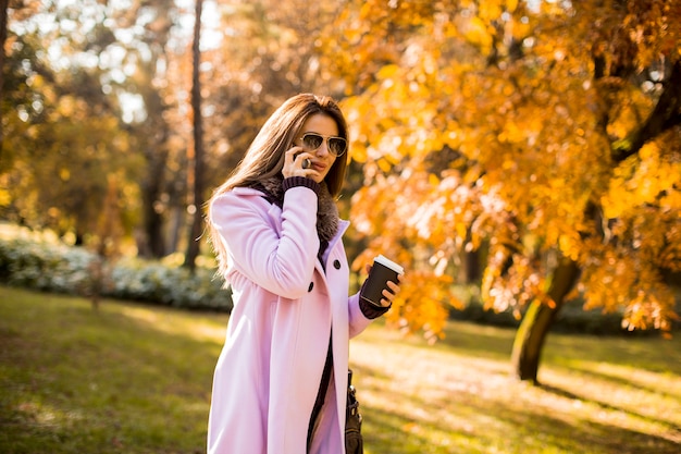 Mulher bonita usando telefone e beber café no parque outono