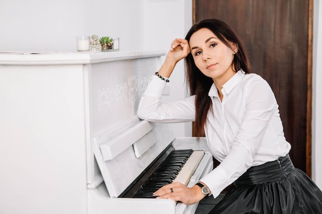 Mulher bonita vestida com camisa branca, tocando piano branco. Lugar para texto ou publicidade